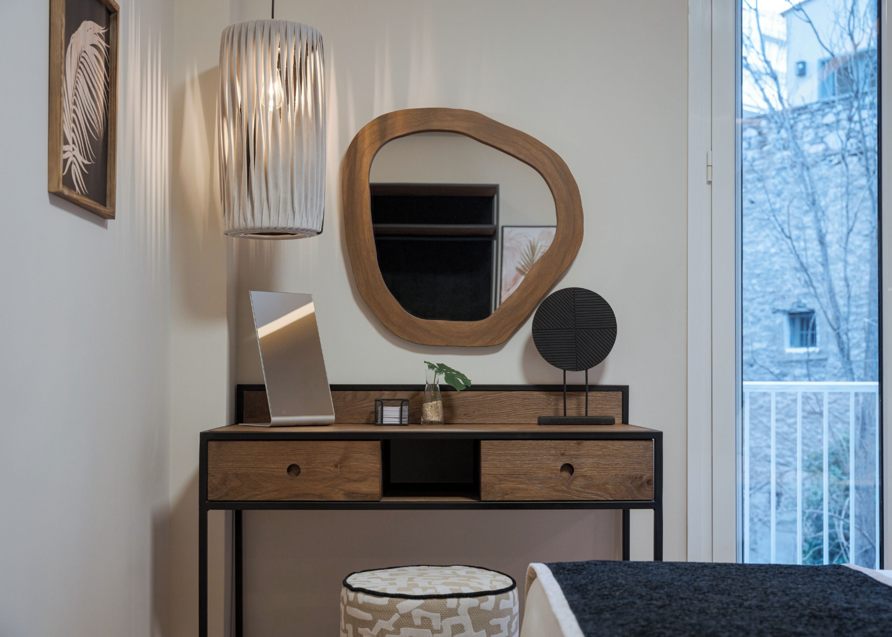 A modern bedroom with a wooden dresser, a mirror, a laptop, and a bedside table with a lamp.
