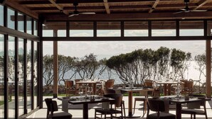 An outdoor dining area with tables and chairs, large windows, and a view of the sea. - Zélia Halkidiki, part of Destination by Hyatt - Adults Only (Nea Propontida)