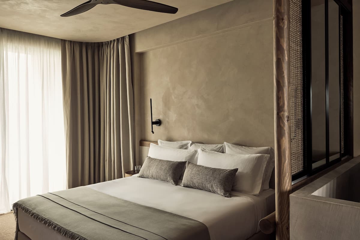 A hotel room with a large bed, a ceiling fan, a window with curtains, and a wooden headboard.