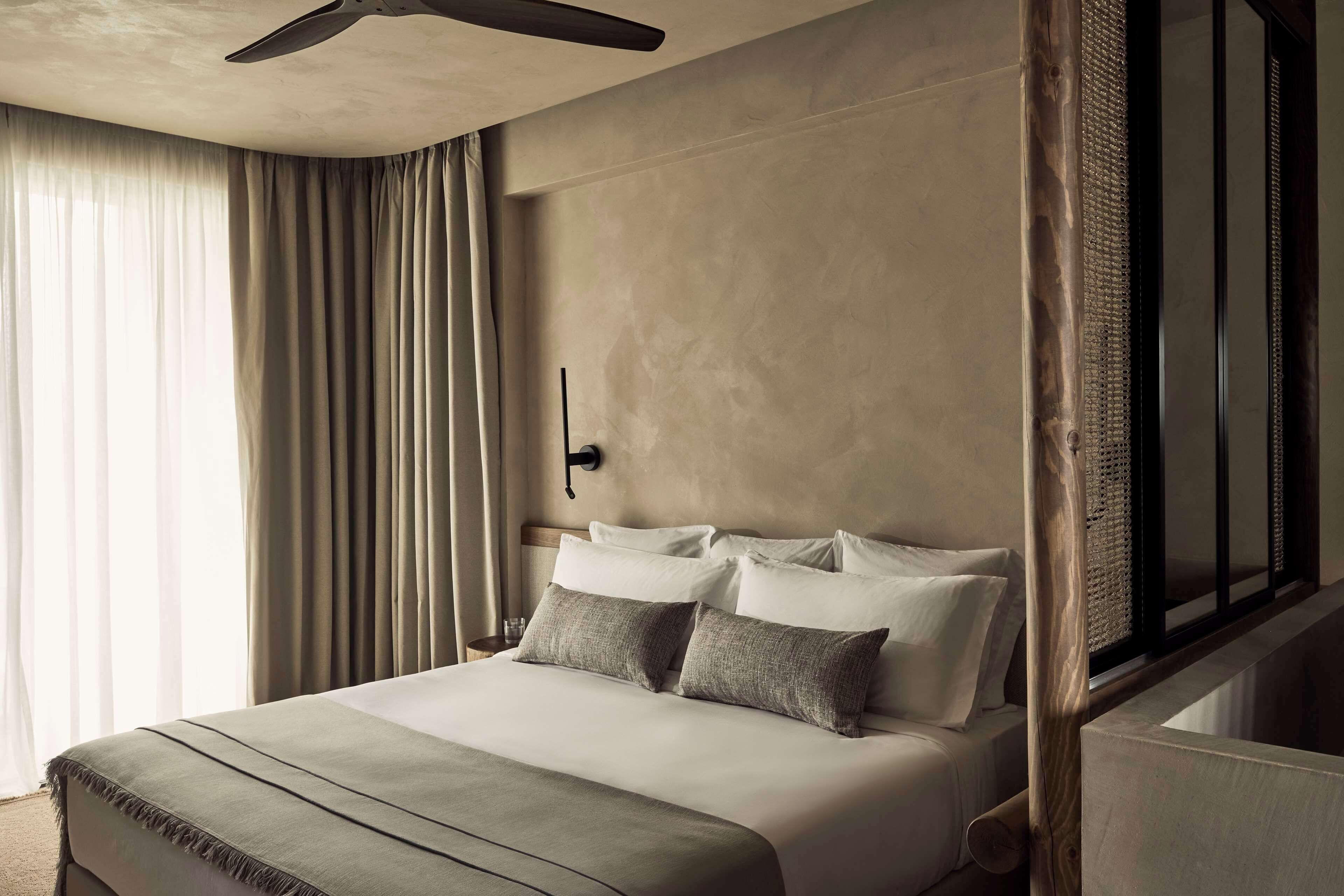 A hotel room with a bed, curtains, a ceiling fan, and a large window.