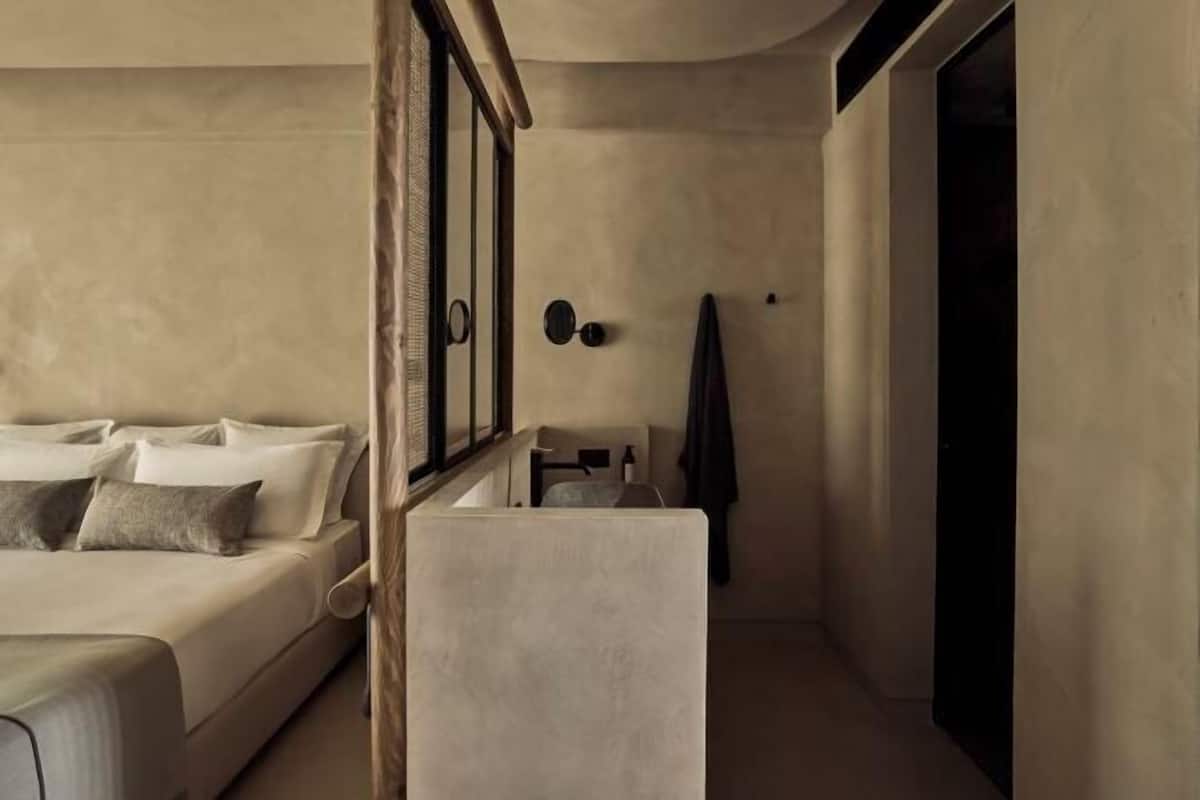 A bedroom with a bed, a small table, a chair, a coat rack, and a door.