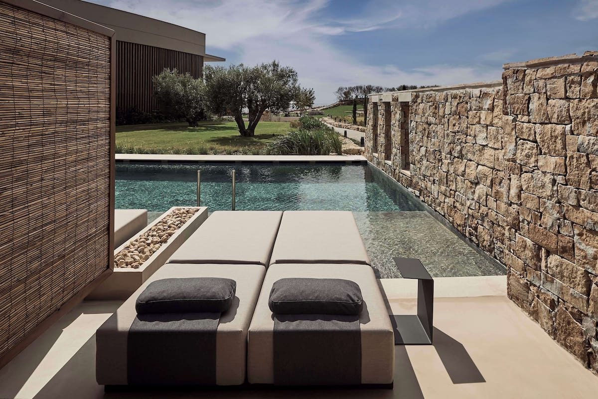 A modern outdoor pool area with lounge chairs and a stone wall.
