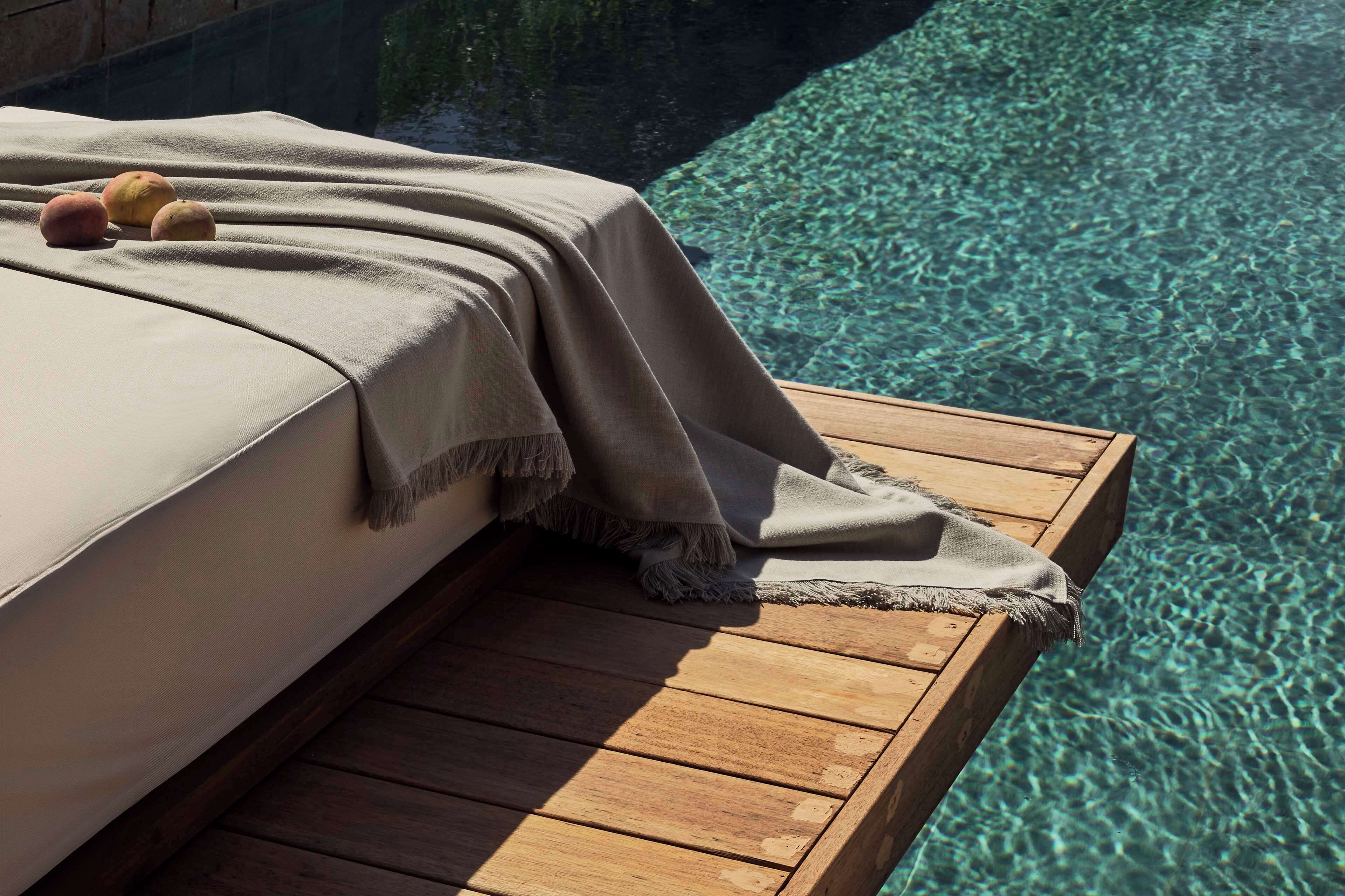 Terraza de madera con una cama y una manta, con vista a aguas cristalinas.