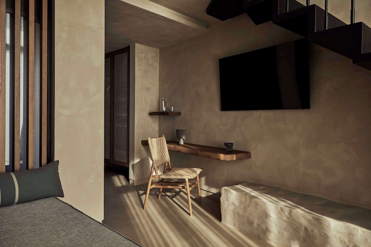 A modern interior with a wooden chair, a bench, a shelf with decorative items, and a staircase.