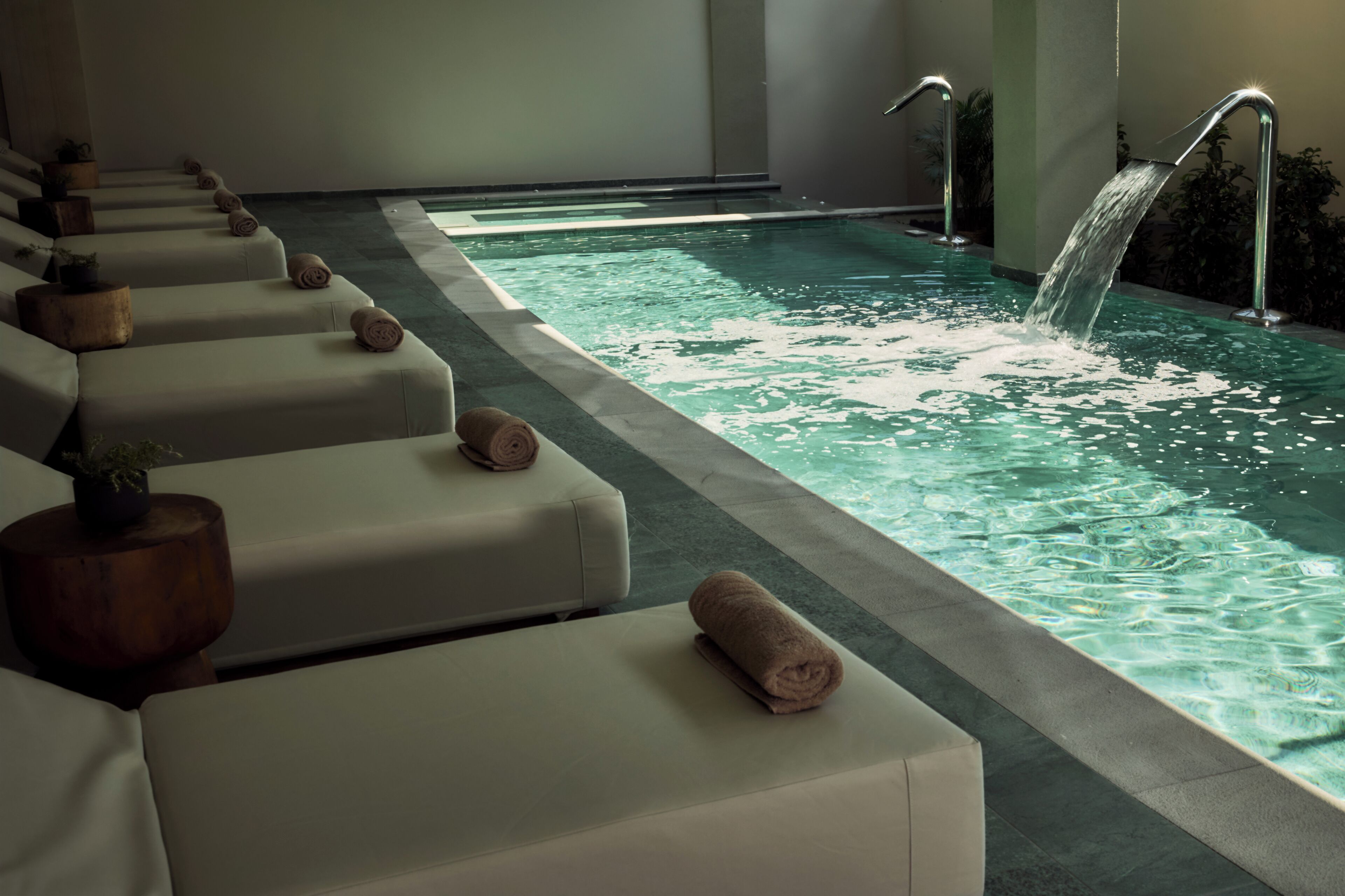 Un área de spa con una piscina larga, múltiples sillones de descanso y una fuente de agua.