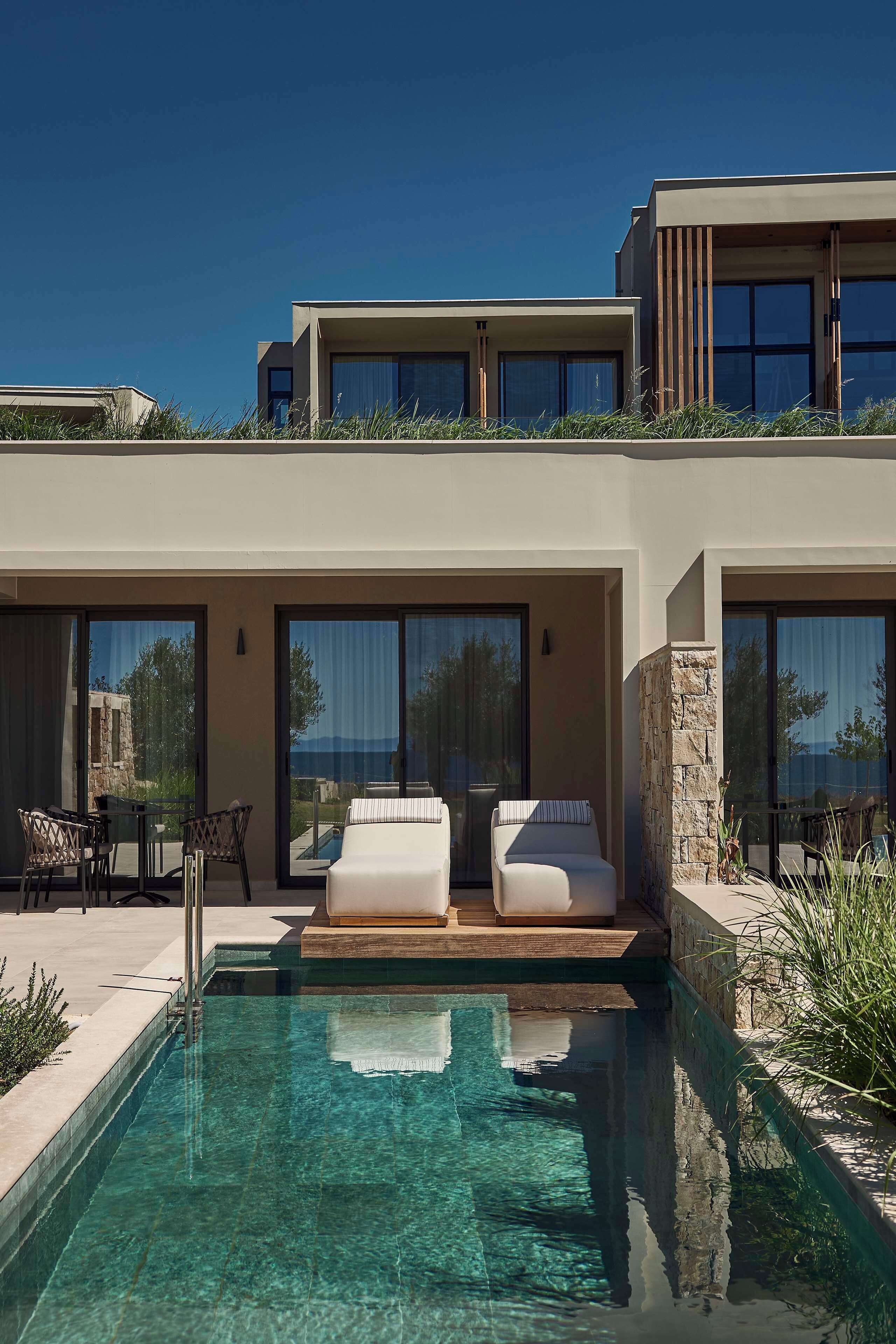 Un hotel moderno con piscina, asientos exteriores y amplias ventanas.