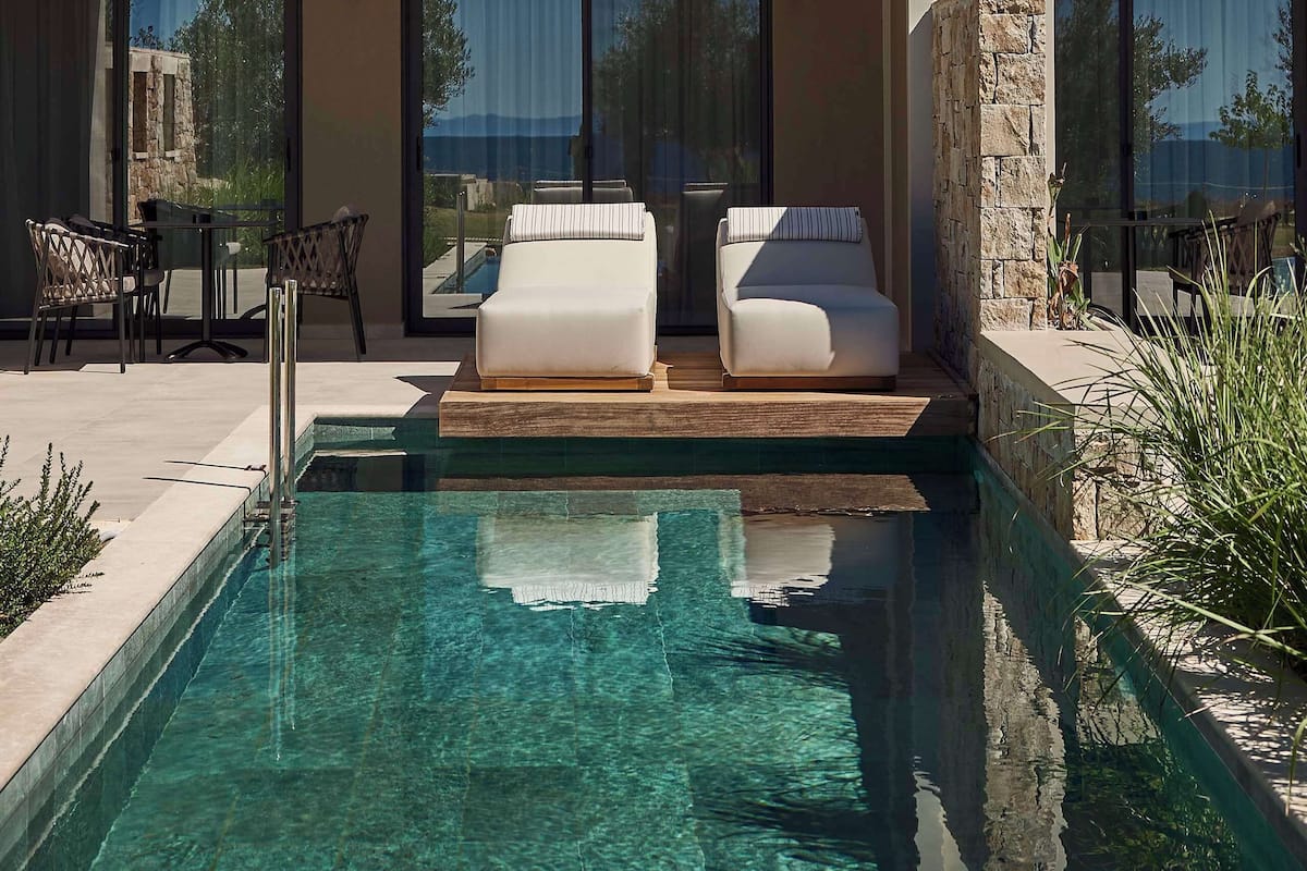 A modern hotel with a pool, outdoor seating, and large windows.