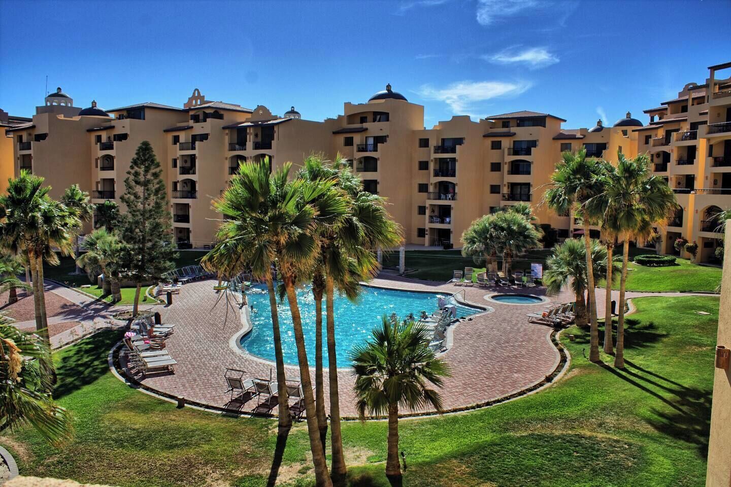 Ein Hotel mit einem zentral gelegenen Schwimmbad, umgeben von Palmen und Liegestühlen.
