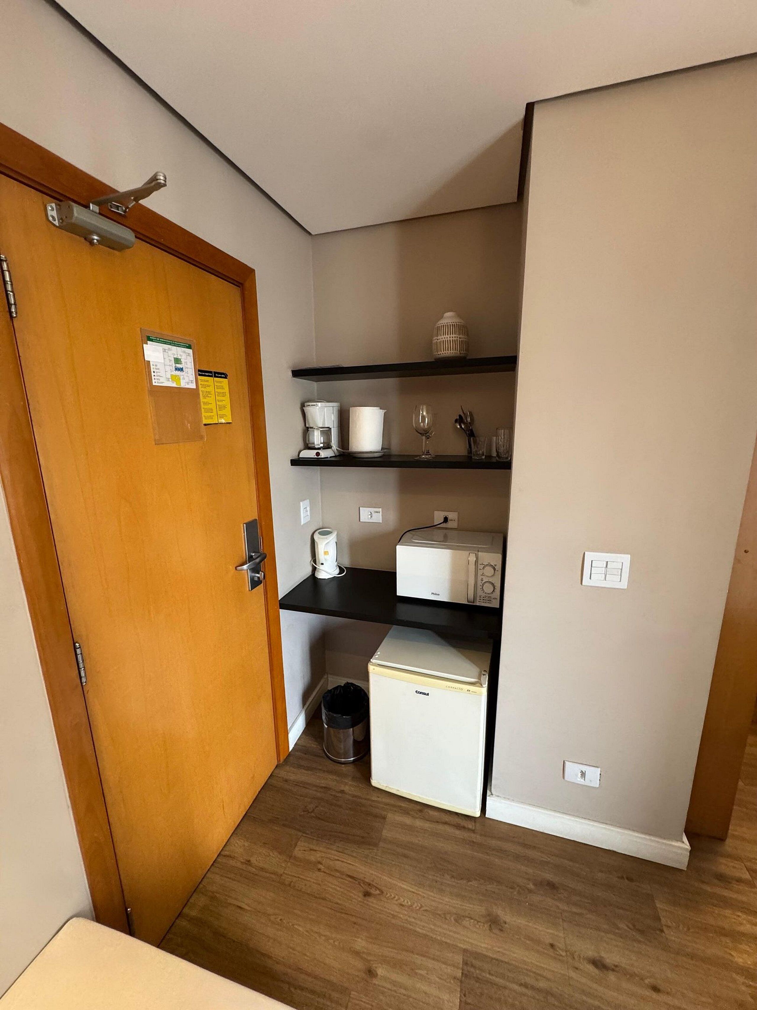 A compact kitchenette with a refrigerator, microwave, coffee maker, and a small trash bin.