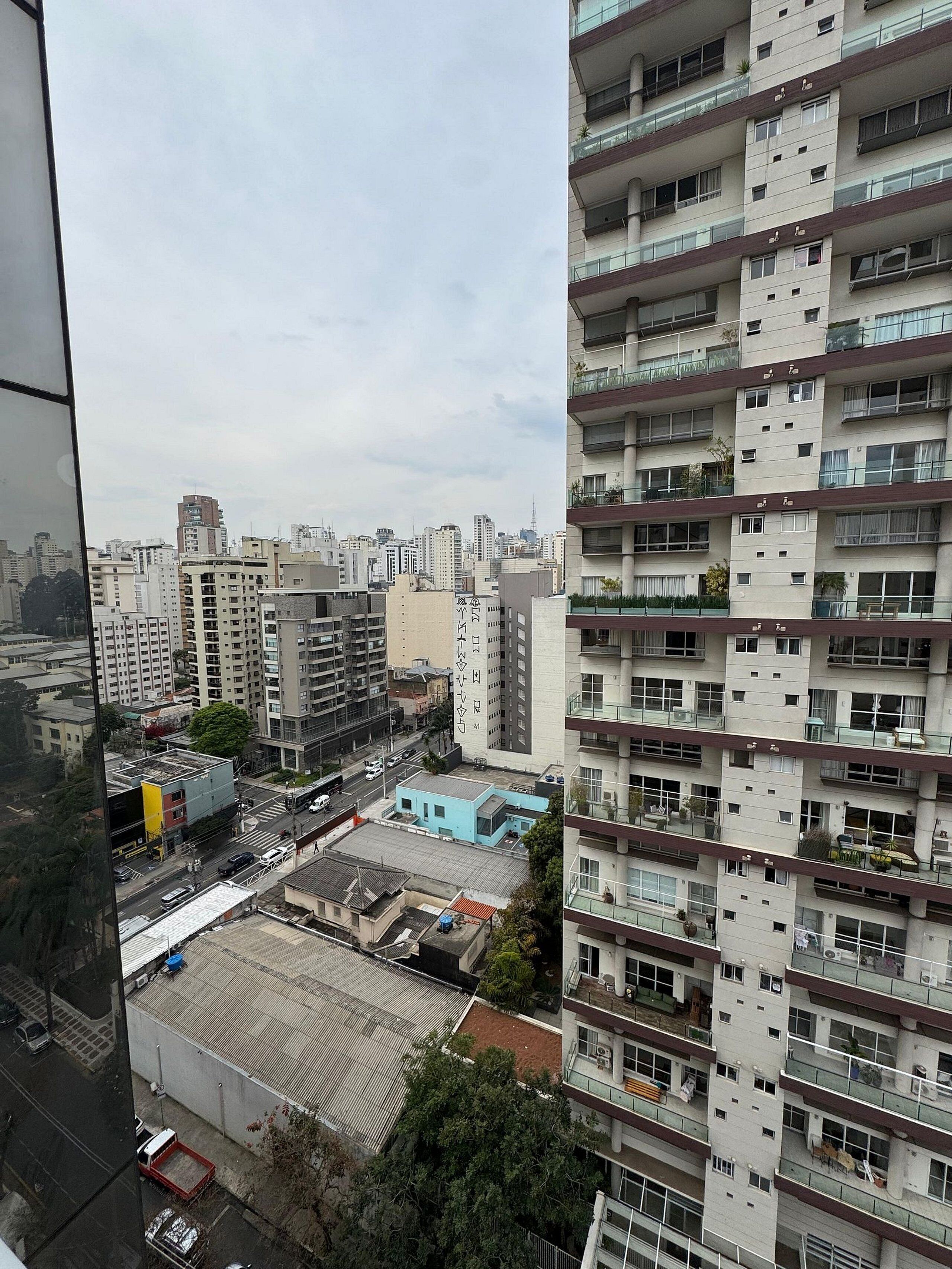 A high-rise building with multiple balconies, a parking area, and a view of the cityscape.