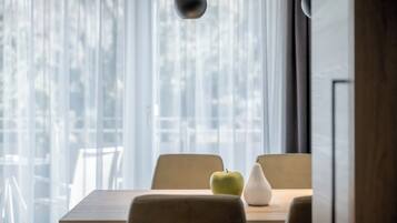 A dining area with a table, chairs, a hanging light fixture, and a view through sheer curtains.