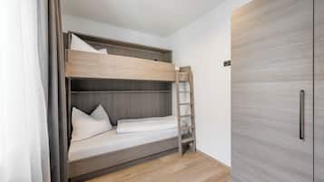 Una cama litera con escalera, un armario y suelo de madera.