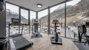A gym with treadmills, an elliptical, and a stationary bike, large windows with a mountain view. - GREEN.Apartments by Camping Sölden (Soelden)