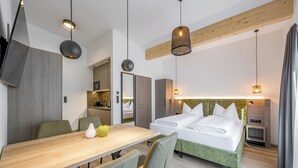 A modern hotel room with a wooden dining table, a bed with green headboard, and pendant lighting. - GREEN.Apartments by Camping Sölden (Soelden)