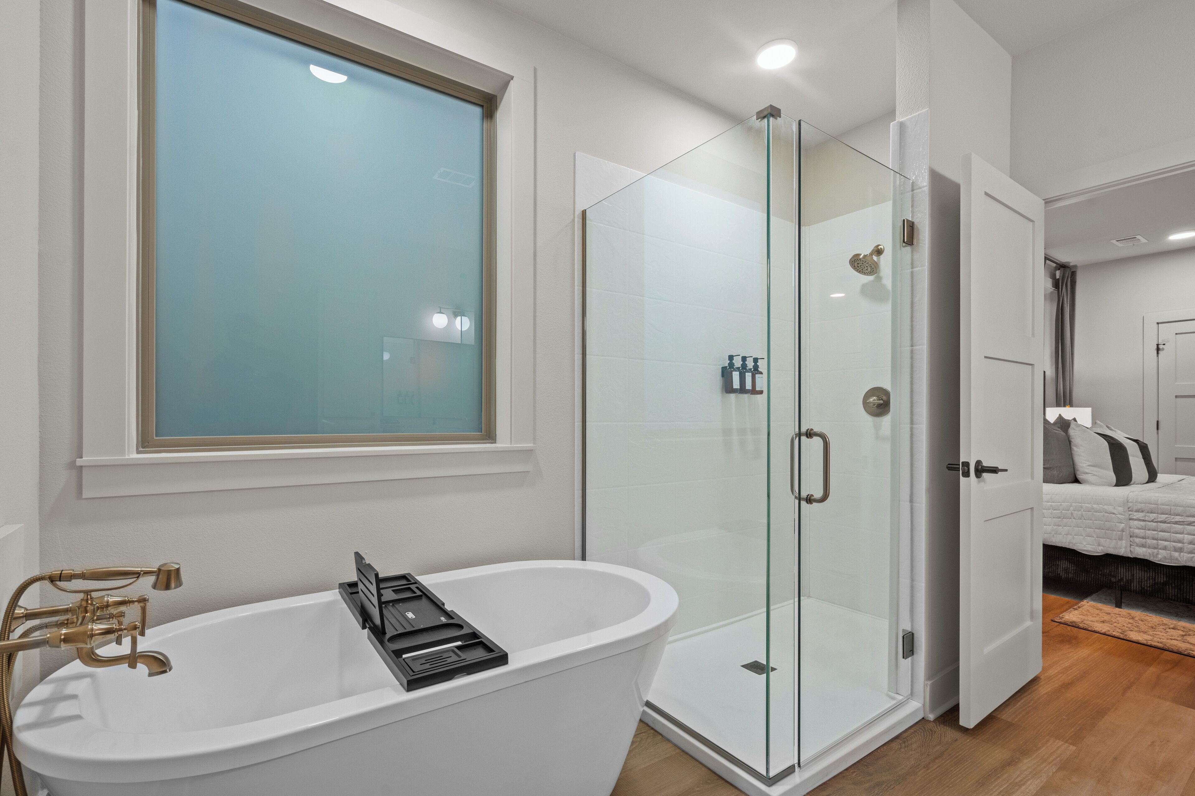 A modern bathroom with a freestanding bathtub, a glass-enclosed shower, and a large window above the sink.