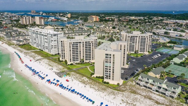 A coastal hotel with multiple high-rise buildings, a beach with umbrellas, and a marina in the background.
