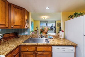 A kitchen with wooden cabinets, a granite countertop, a stainless steel sink, and a white dishwasher. - Ocean View Retreat With Pool and Sauna - Top Floor (Kailua-Kona)
