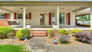 A single-story house with a covered porch, a brick foundation, and a front yard with shrubs and a flag.
