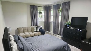 Een slaapkamer met een bed, een bank, een televisie en een dressoir.