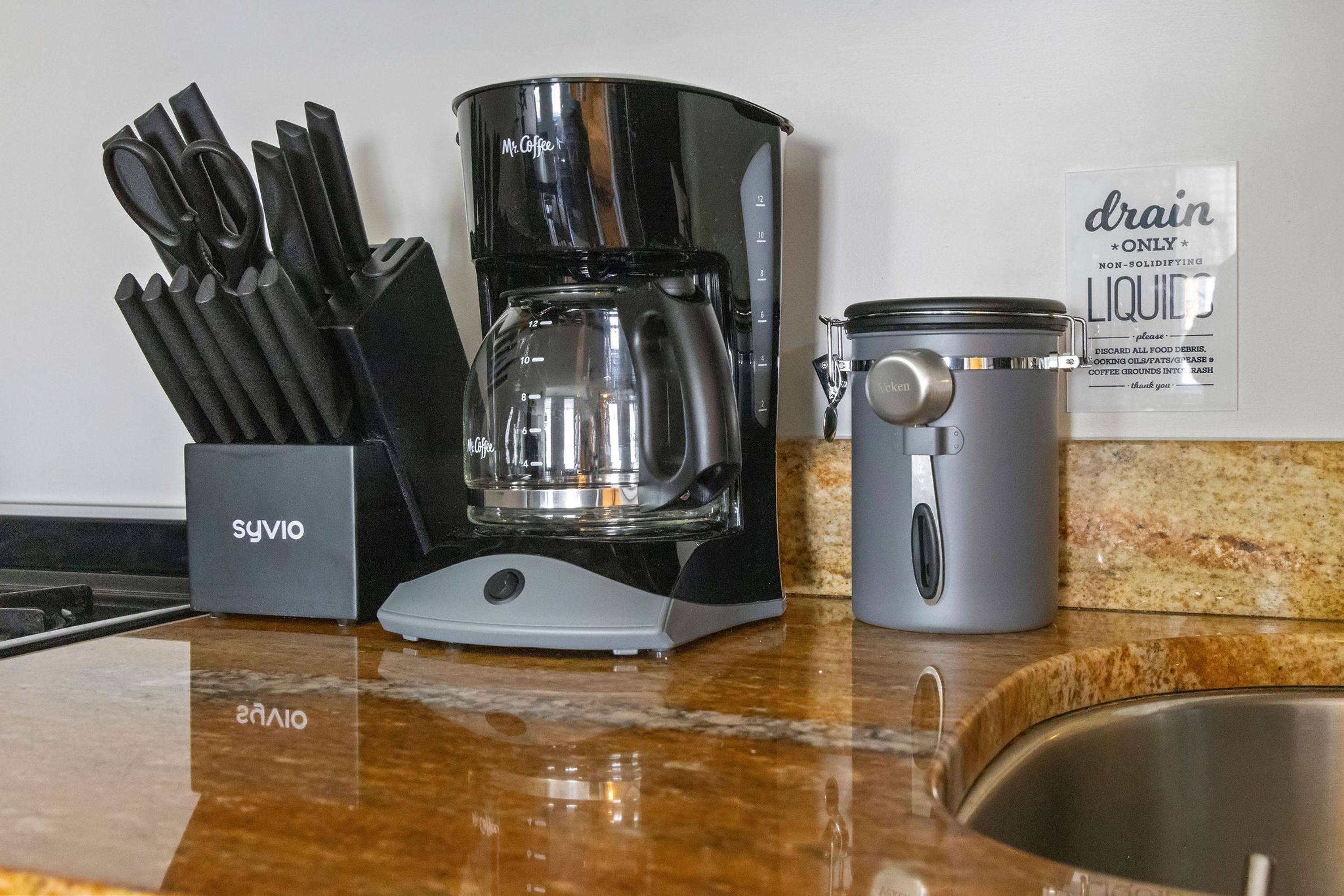 Eine Kaffeemaschine, eine Tasse und ein Messerset auf einer Küchenarbeitsplatte.