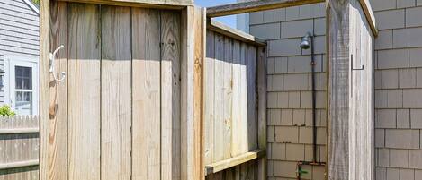 Une cabine de douche extérieure en bois, dotée d’un robinet en métal et d’un tuyau d’arrosage.