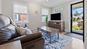 Una sala de estar con un sofá de cuero, una mesa de centro, un televisor sobre un mueble de madera y una puerta que da a un balcón.