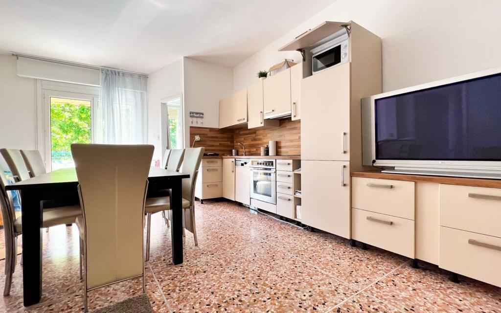 Una cocina moderna con comedor, que incluye un televisor grande, armarios de madera y piso de baldosas.