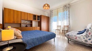 Une chambre à coucher avec un lit, un bureau avec une lampe, une chaise, une armoire et une fenêtre avec des rideaux.