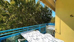 Un balcon avec une balustrade bleue et une table recouverte d’une nappe à motifs de poissons.