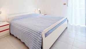 Een slaapkamer met een bed, nachtkastje, lamp en raam met gordijnen.