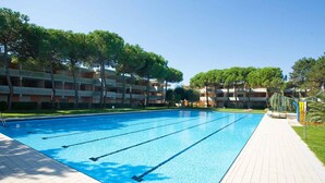 Ein Schwimmbecken mit klarem, blauem Wasser, umgeben von einer gefliesten Terrasse und Bäumen.