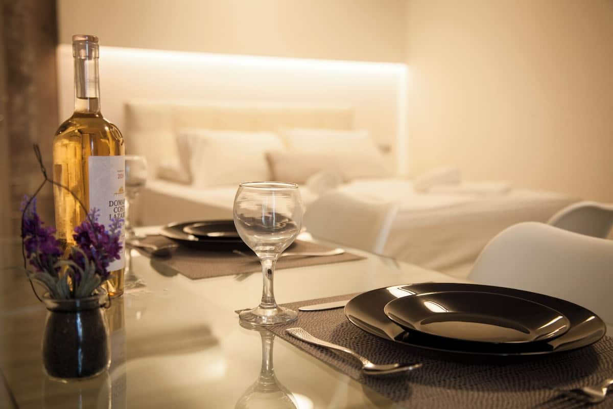 Une chambre d’hôtel avec une table à manger soigneusement dressée, une bouteille de vin et un vase rempli de fleurs.