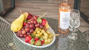 Une table à manger avec un plateau de fruits, une bouteille de vin et un verre. En arrière-plan, on aperçoit un canapé vert et une table basse en bois.
