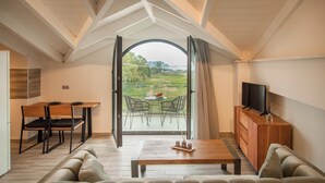 Un salon moderne avec un grand canapé, une table basse en bois, un coin repas avec des chaises, un téléviseur posé sur un meuble en bois et une vue sur un terrain de golf, visible à travers une porte vitrée.