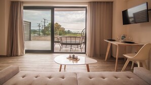 Une chambre d’hôtel moderne dotée d’une grande porte-fenêtre coulissante donnant sur une terrasse extérieure, d’un téléviseur à écran plat fixé au mur, d’une table basse ronde et d’un canapé.