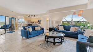 Ein großzügiger Wohnbereich mit einem runden Couchtisch, zwei blauen Sofas und Blick auf die Stadt durch ein großes Fenster.