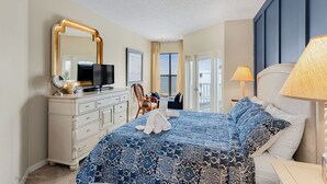 Ein Hotelzimmer mit einem großen Bett, einem Schminktisch, einem Fernseher und Meerblick durch das Fenster.