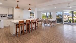 A modern kitchen with white cabinetry, a central island with bar stools, and a dining area with a table and chairs. - 37 Victor Avenue on the Forster Keys (Forster)