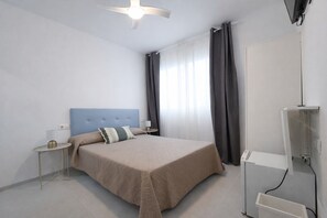 Habitación de hotel con cama, mesita de noche, lámpara, ventilador de techo, televisor y armario.