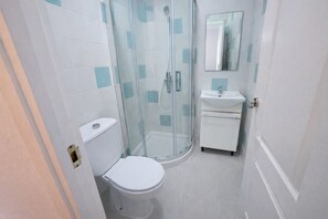 Un baño con inodoro, ducha con mampara de vidrio y lavabo con espejo.