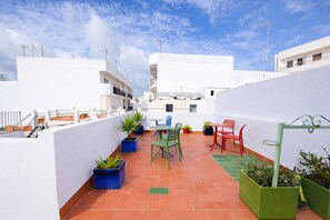 Terraza en la azotea con una mesa y sillas, rodeada de plantas en macetas y un tapete verde.