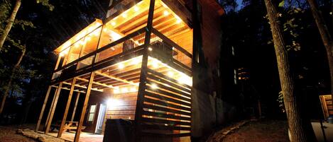 A two-story wooden cabin with a balcony and a hot tub area.