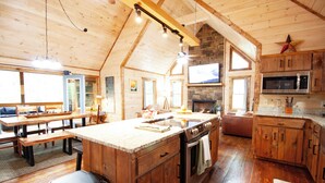 A spacious kitchen with wooden cabinets, a large island, and a stone fireplace. - Fall Sale! Luxury Cabin. Top Location. Hot Tub Game Room EV Firepit (Blue Ridge)