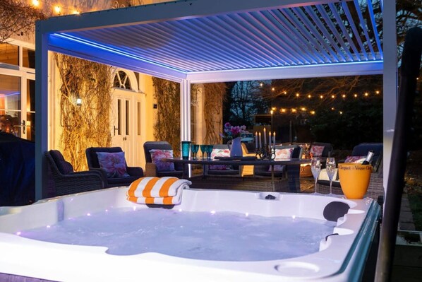 An outdoor hot tub area with a pergola overhead, surrounded by lounge chairs and a table with drinks. - Luxury Georgian Country House With Hot Tub (Ross-on-Wye)