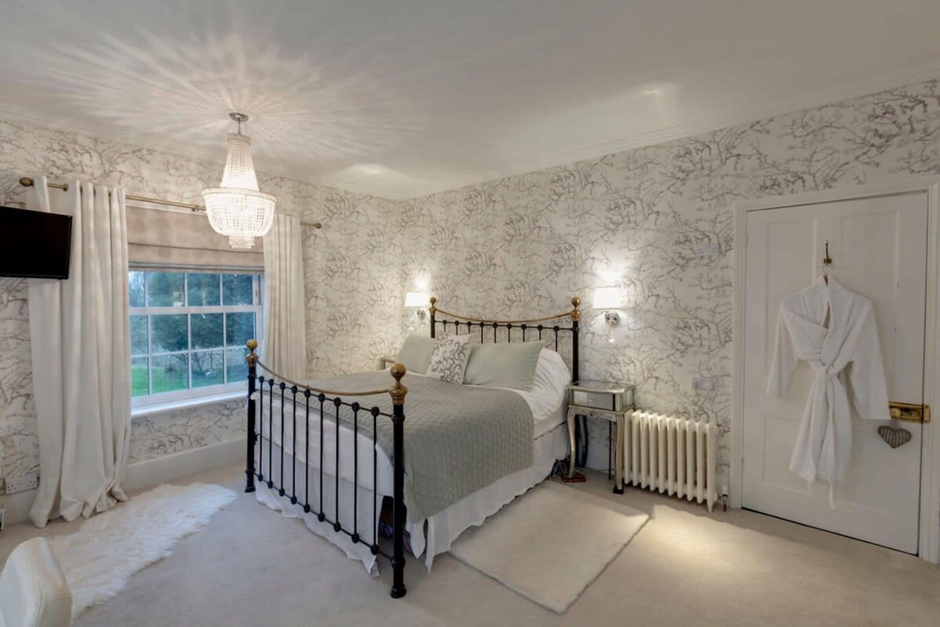 A bedroom with a bed, a radiator, a window, and a door with a robe hanging.
