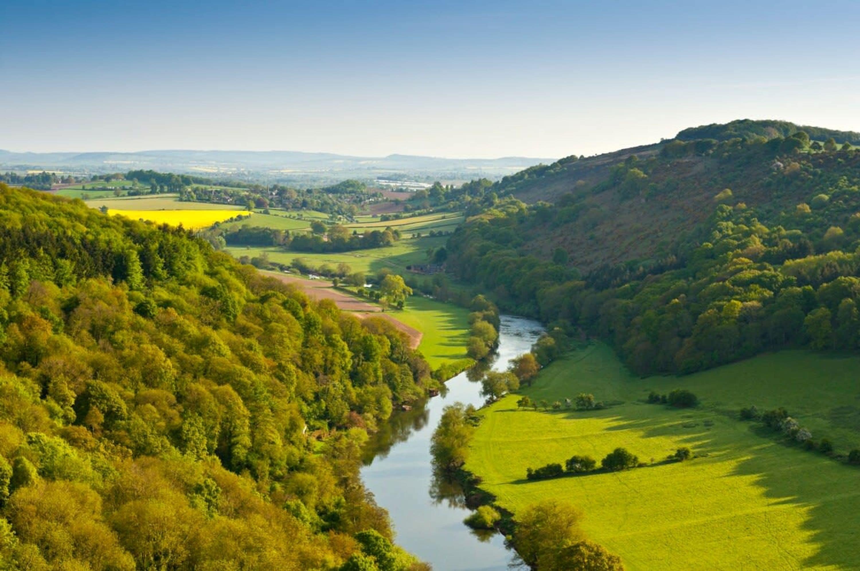 Un río serpentea por un valle con campos verdes exuberantes y una colina a la derecha.