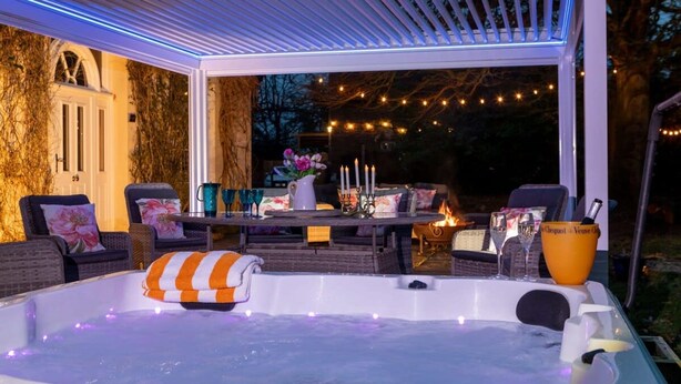 Un bain à remous avec une serviette à rayures, entouré de meubles d’extérieur et illuminé de guirlandes lumineuses.