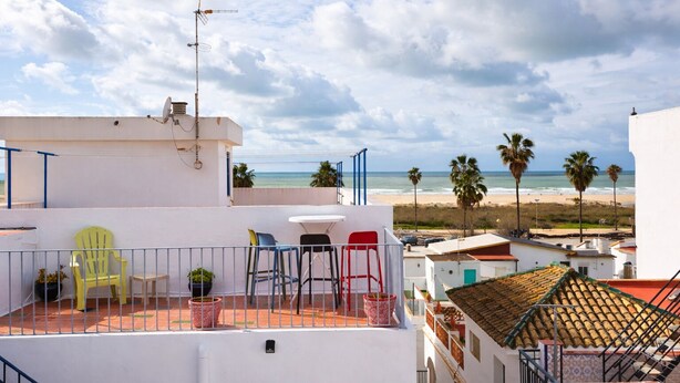A rooftop terrace with a view of the beach, featuring a white building, a satellite dish, and several chairs.