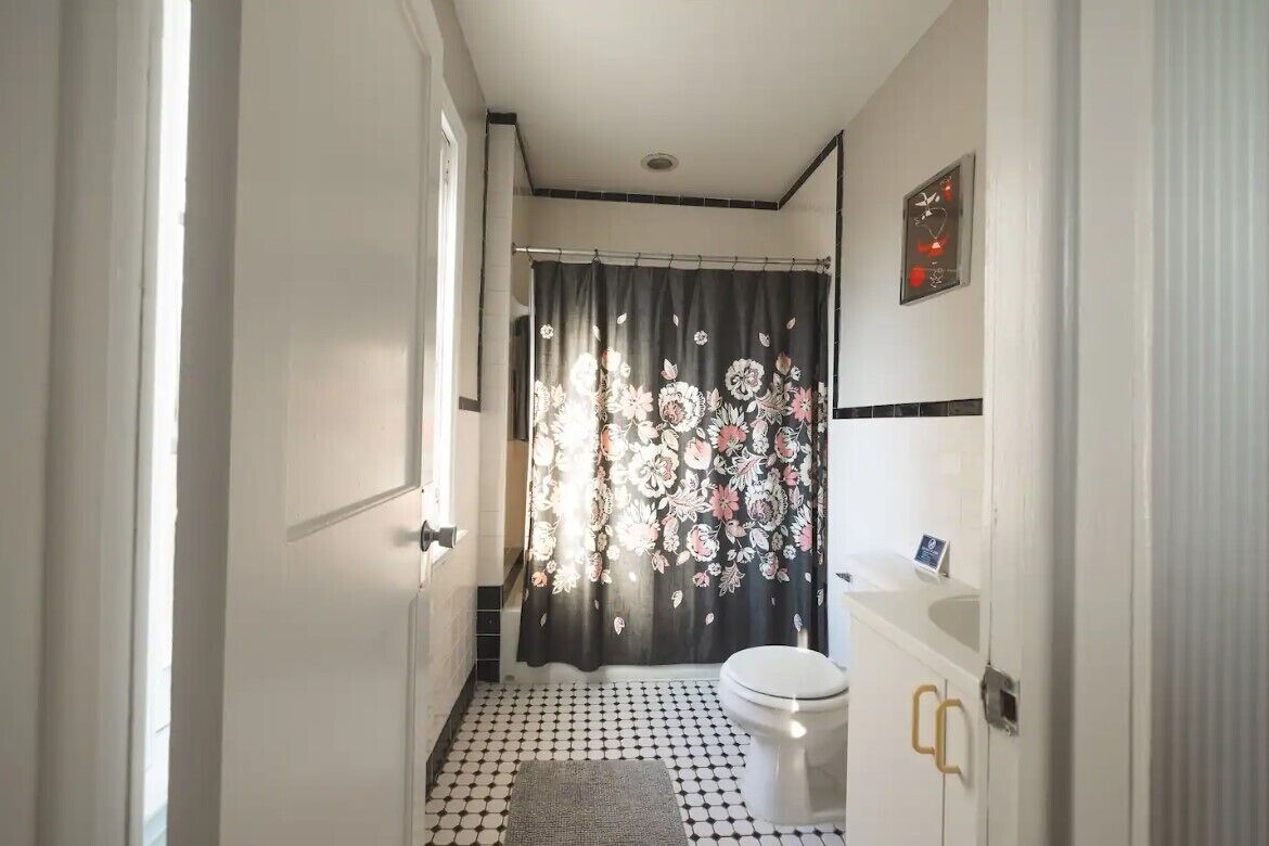 A narrow bathroom with a toilet, a sink, and a shower curtain with a floral pattern.