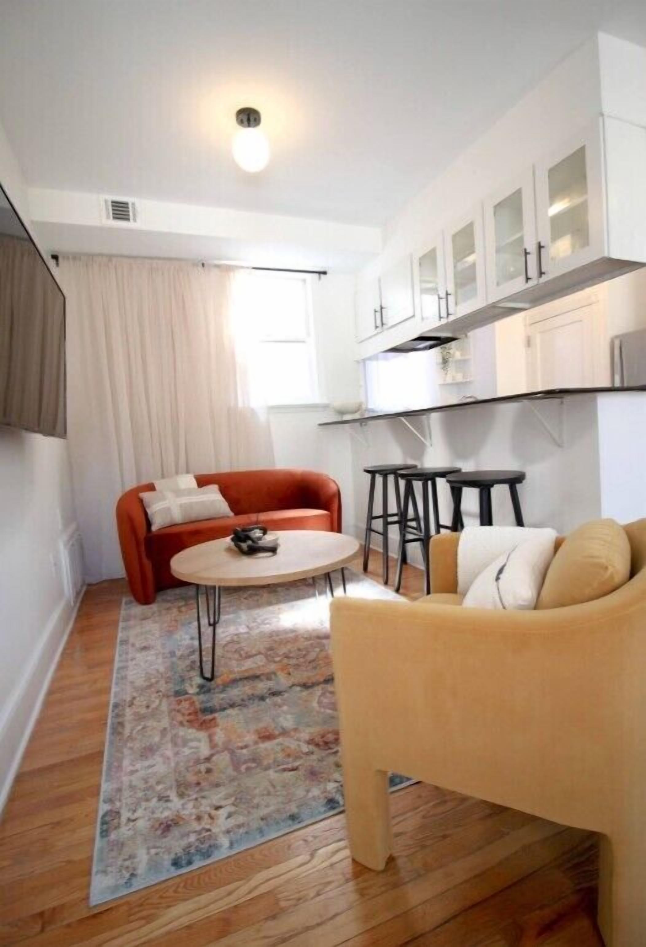 Un espacio habitable compacto con kitchenette, dos sofás, una mesita de centro y una alfombra estampada.